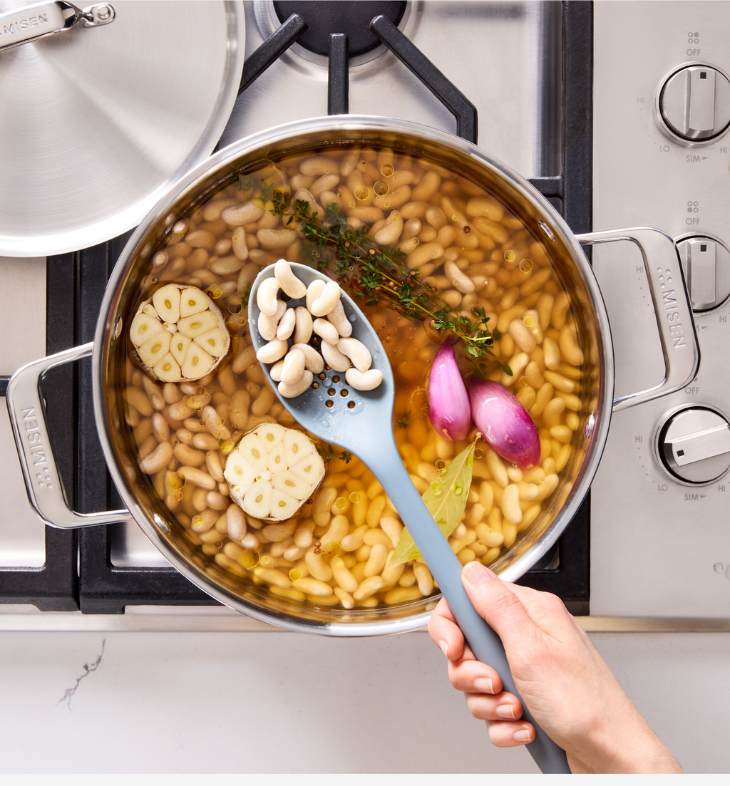 Cooking white beans with garlic, shallots, thyme, and bay leaf in a stainless steel pot on gas stove